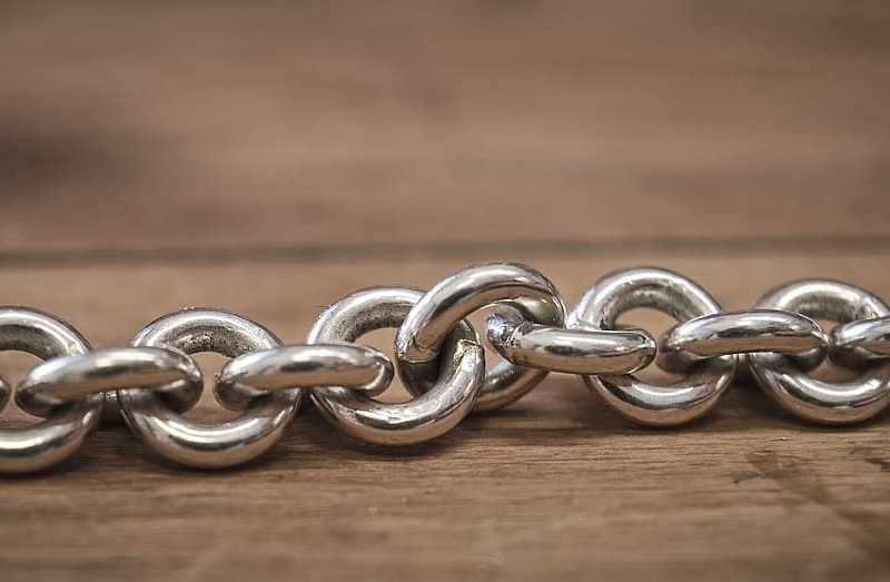 a chain of circular silver links rest on a wooden surface