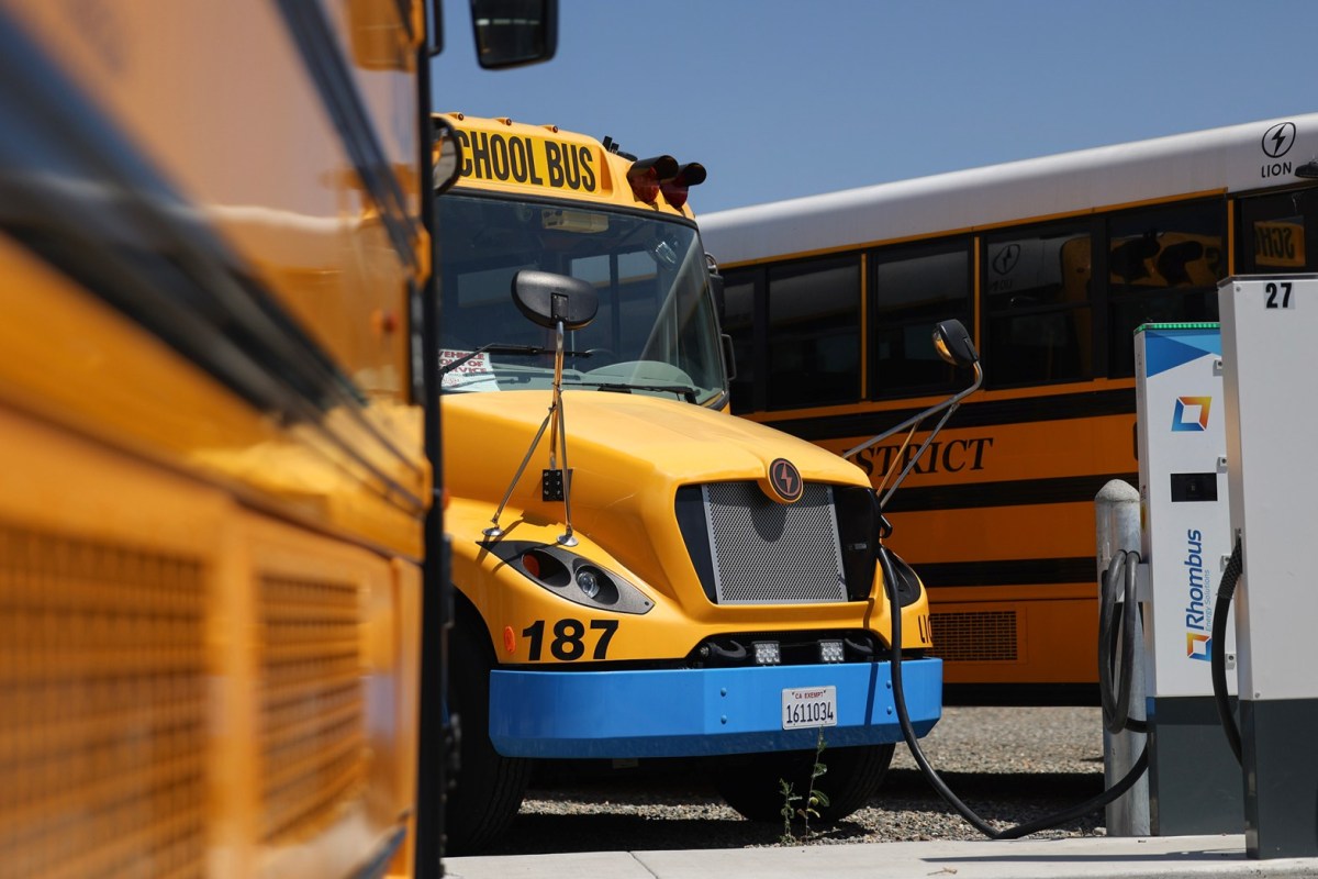 A yellow electric school bus is plugged into a charging station.