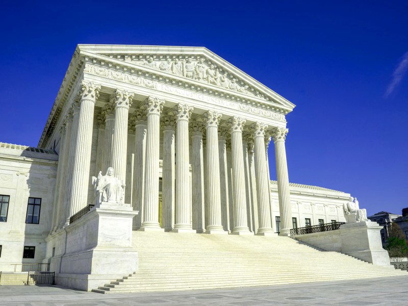 The U.S. Supreme court building has tall pillars and is flanked with two statues of judges.