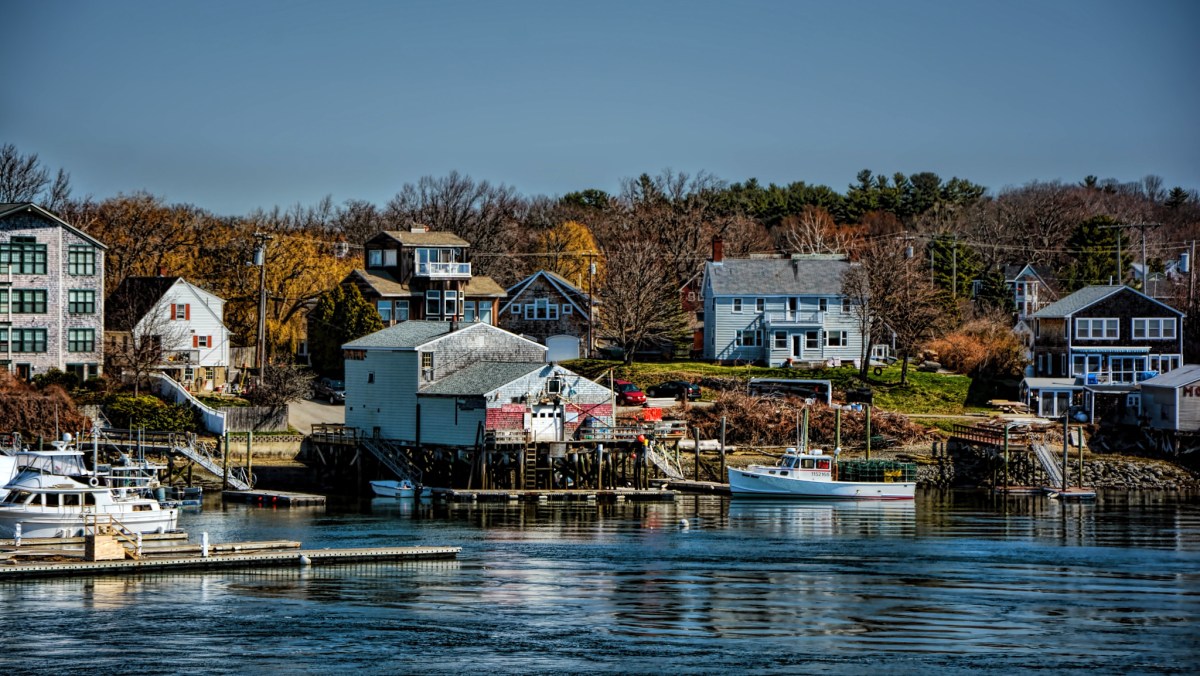 Homes line the rocky coast of Kittery, Maine. Two boats and docks are also visible.