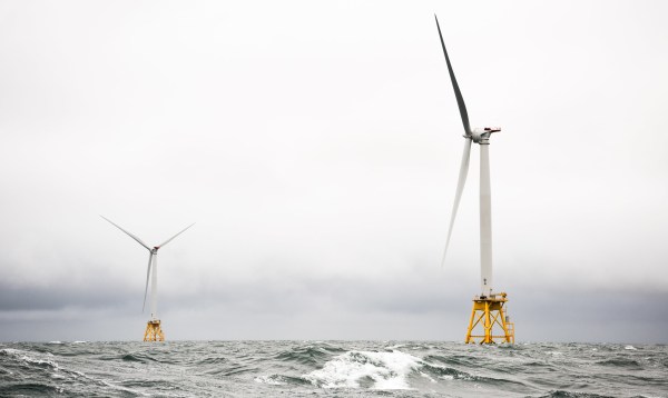 Two offshore wind turbines sit in grey churning water against a great sky