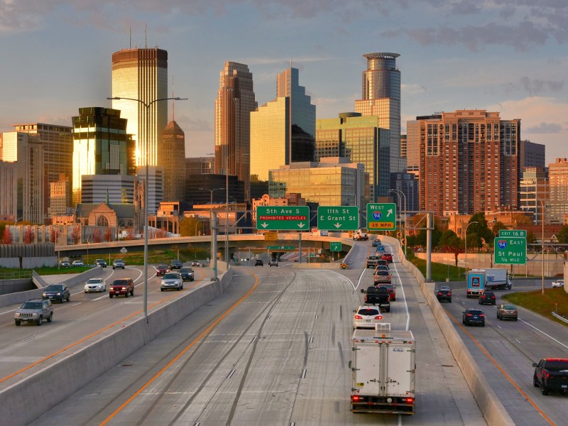 A massive width of highway approaches the downtown Minneapolis skyline