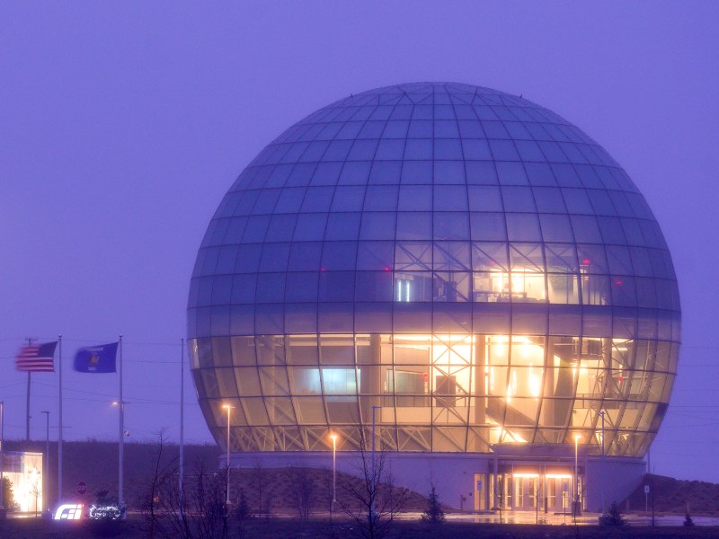 A giant glass orb of a building glows in an indigo sky as the sun sets.