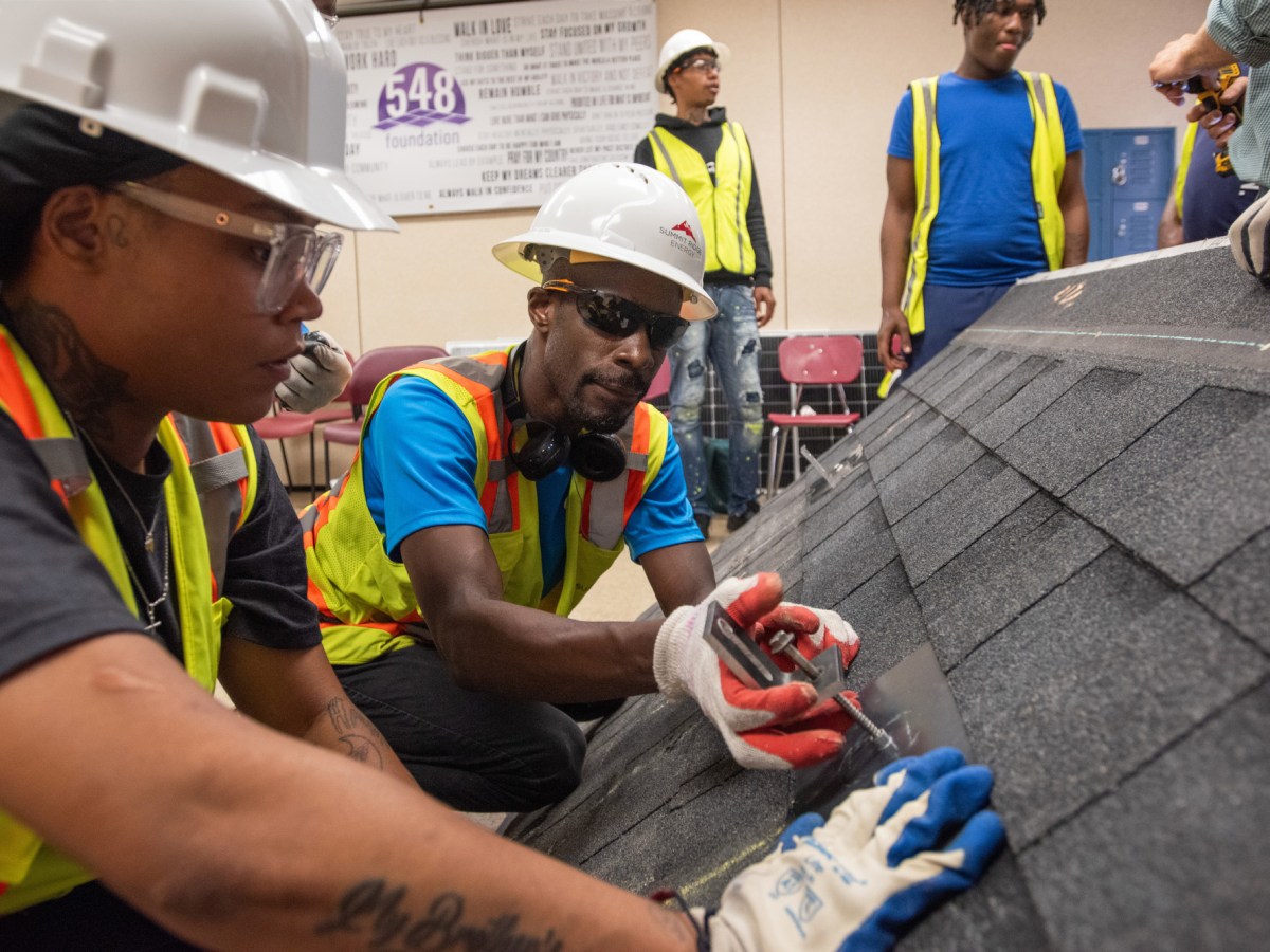 Students wearing safety gear practice installing brackets on a mockup of a pitched roof.