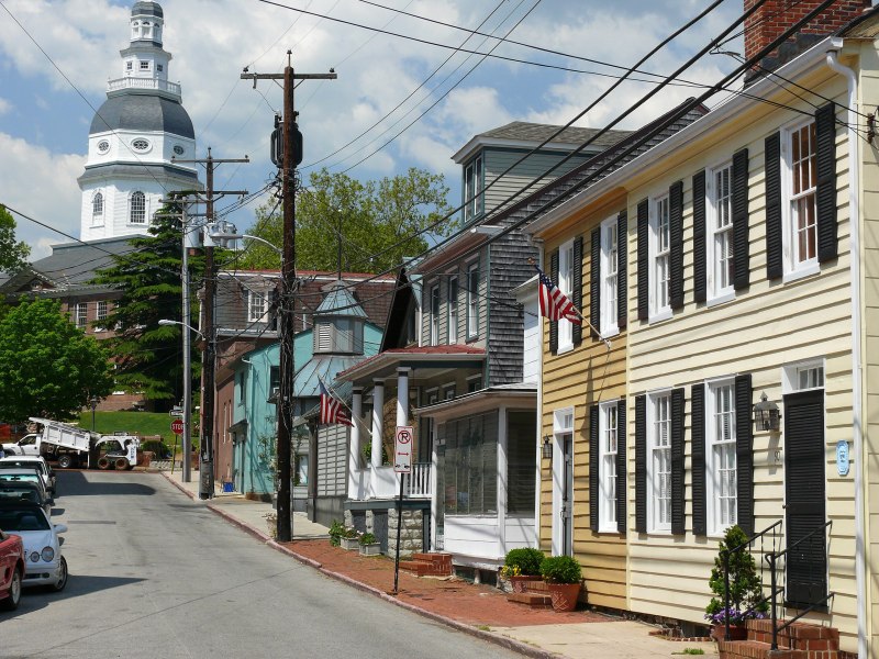 The Maryland State House is viewed down a narrow street with older, two-story buildings and power lines.