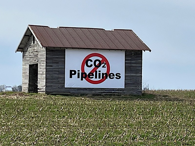 A banner with the words CO2 Pipelines and a red slash hangs from a barn in a cornfield