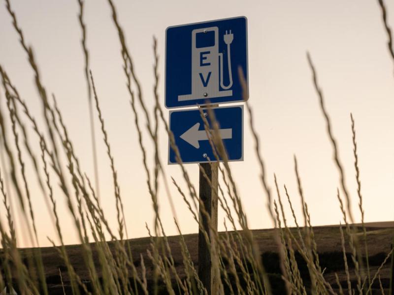 A sign in a field points to an electric vehicle charging station.