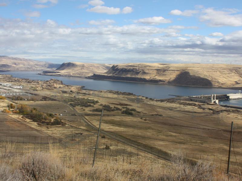 A dam is visible on the Columbia River and surrounded by brownish grass