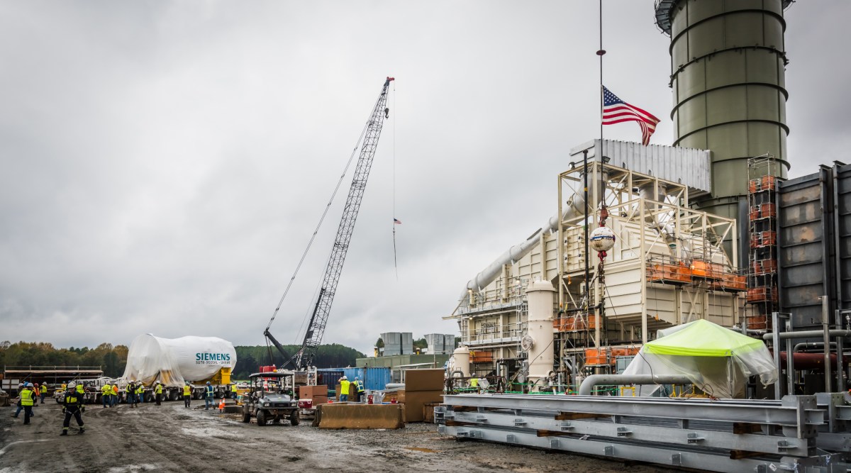 A crane and workers at a natural gas power plant as a new gas turbine is delivered.