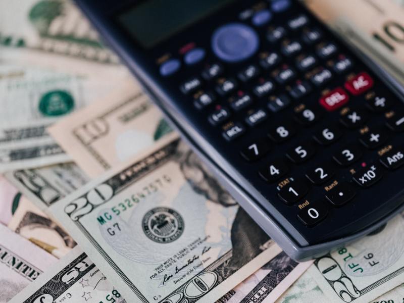 A calculator rests on top of a messy pile of U.S. bills.