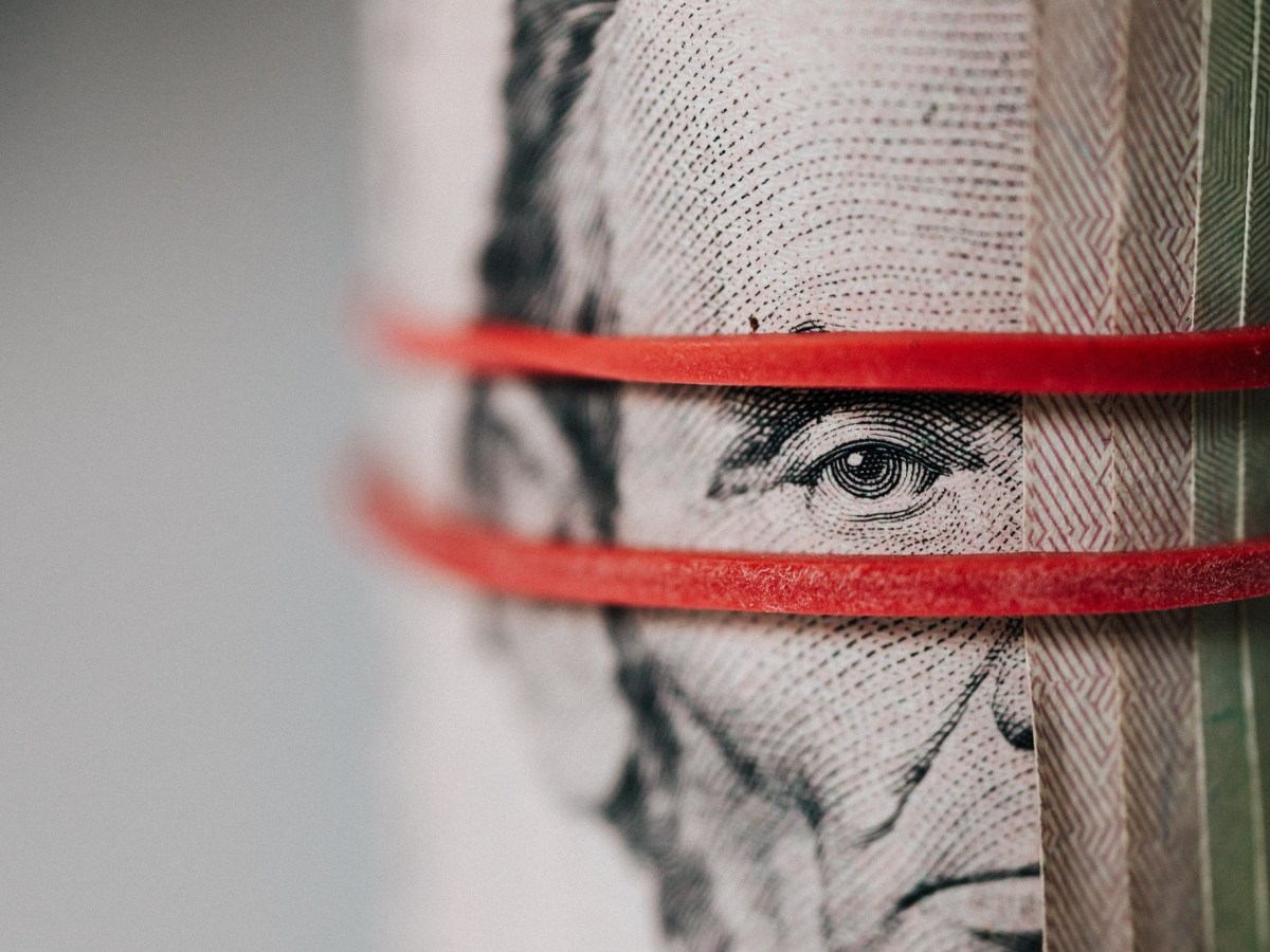 A roll of bills secured by a pair of red rubber bands, between which peers the printed eye of Abraham Lincoln.