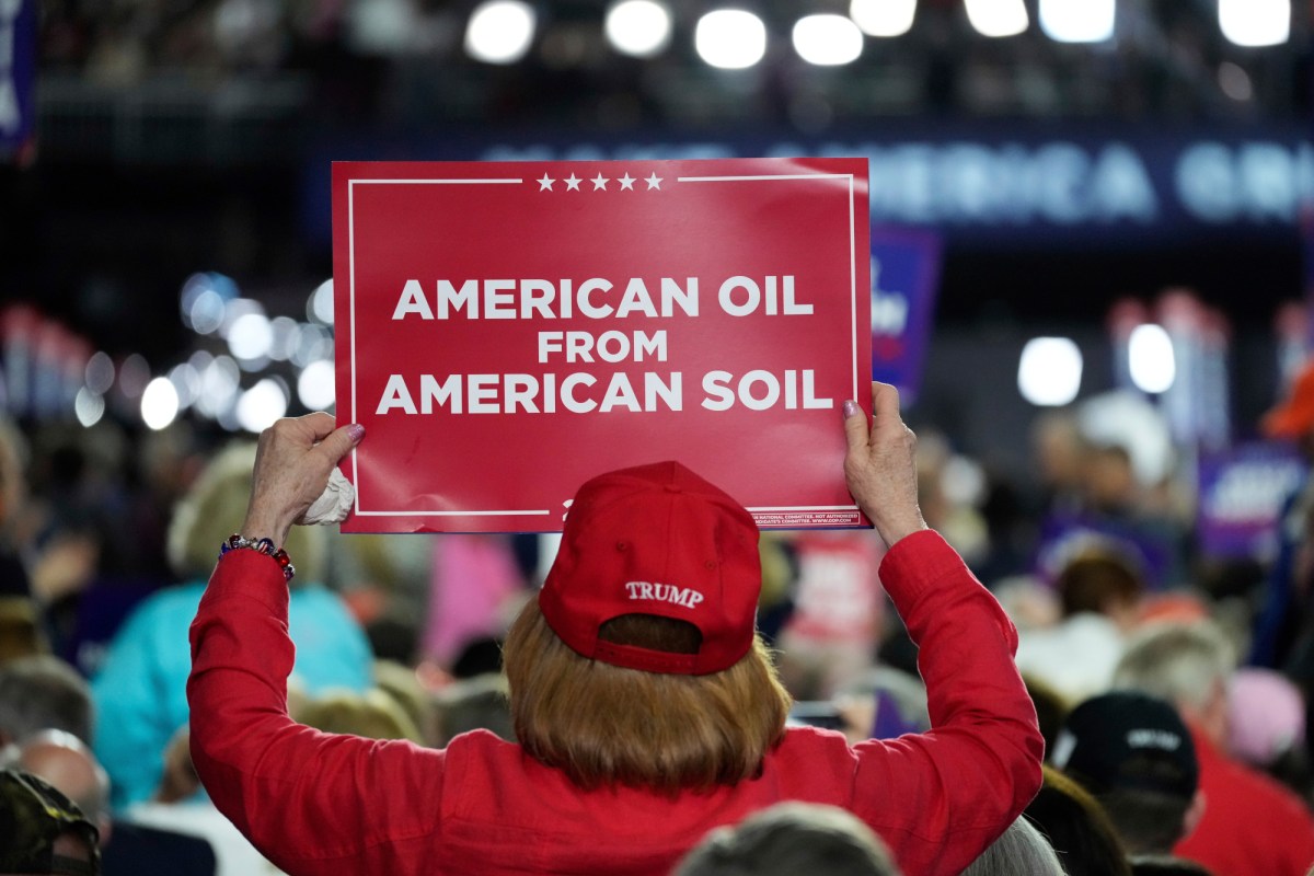 A person wearing a red Trump hat holds a sign reading "American oil from American soil" at the Republican National Convention.