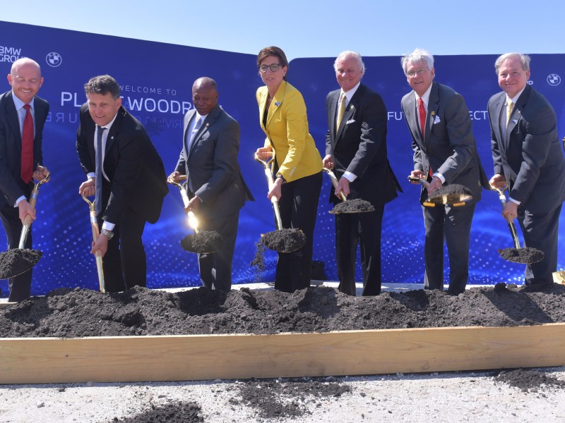 Executives and politicians in suits dig dirt with ceremonial shovels at a groundbreaking for a BMW battery plant in South Carolina.