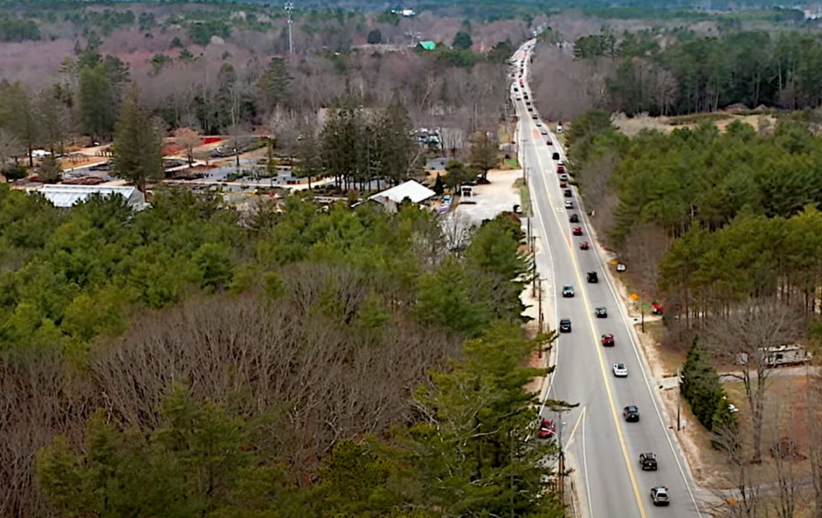 A video still showing heavy traffic on a two-lane highway through a wooded area of Maine that also features homes and commercial development.